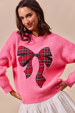 Front detail of the SO ME pink holiday sweater's large red-and-black plaid bow.