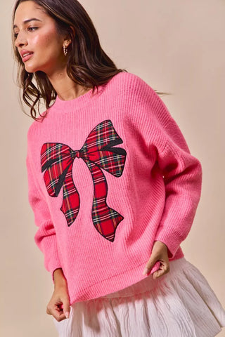 Side-front view of the SO ME pink sweater with a red plaid bow and ribbed hem.