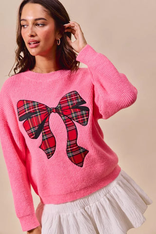 Close view of the SO ME pink sweater's plaid bow design and ribbed neckline.