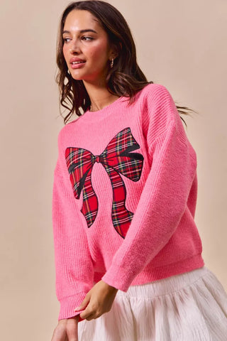 Side view of the SO ME pink plaid-bow sweater showing its long sleeves and ribbed hem.