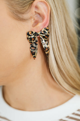 Bow'd & Bold leopard-print bow earrings, on-ear close-up showing the ribbon-bow shape.
