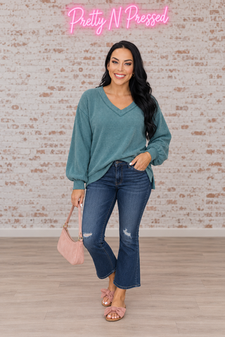 Natalie wearing the dusty teal Doesn't Compare V-neck top with long sleeves, wide cuffs and side-split hem.