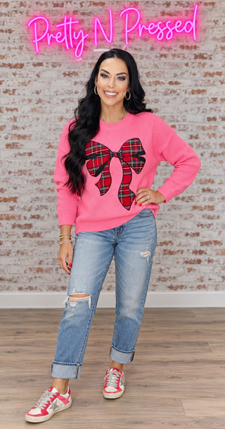Natalie wearing the pink plaid-bow holiday sweater with distressed boyfriend denim and coordinated red, pink and silver sneakers.