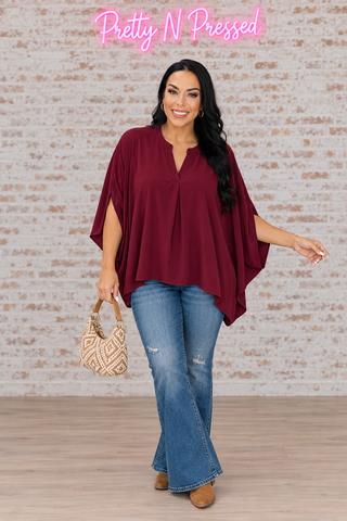 Natalie wearing the wine Universal Philosophy poncho blouse with a split neckline and fluid oversized drape.