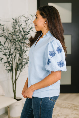 Light-blue That Easy blouse with floral-embroidered sleeves, side view showing the puff sleeve.