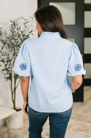 Light-blue That Easy blouse with floral-embroidered sleeves, back view showing embroidered sleeves.