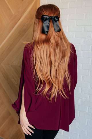 Wine Universal Philosophy poncho-style blouse, back view with black trousers.