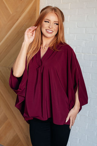 Wine Universal Philosophy poncho-style blouse, front view with V-neckline and draped sleeves.