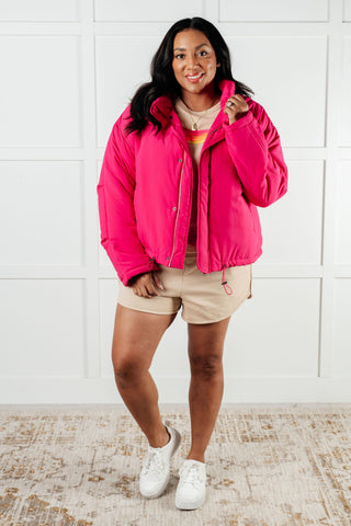 Bright-pink White Birch Warm Regards puffer jacket, full outfit with tan shorts.