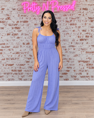 Natalie wearing the Eden elastic-waist jumpsuit in Very Peri, front view with tied shoulder straps and wide legs.
