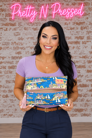 MyKonos Medium makeup bag held by Natalie, with a coastal village print, pink center zipper and tassel.